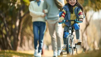 A little Girl Rides Her Bicycle While Her Parents Watch Happily From a Distance