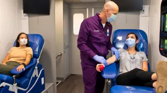 Phlebotomist preparing donor in AdventHealth Bloodmobile while both wear masks.