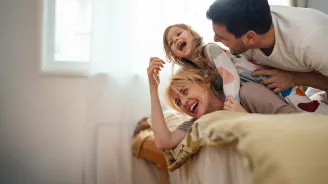 A mother and father play with their child in a bedroom.