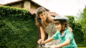 A mother helps her child learn to ride a bike.