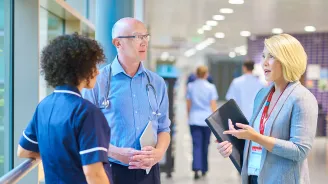 A CPE Pastor Speaks with a Doctor and Nurse in the Hallway of a Hospital.