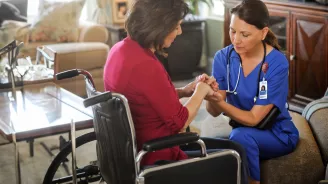 Woman in a wheelchair praying with a home care nurse.
