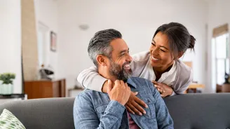 A man and woman laugh together in their living room. 