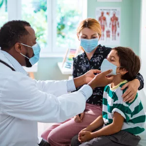 A pediatrician examining a young boy while his mother comforts him on the examination table.