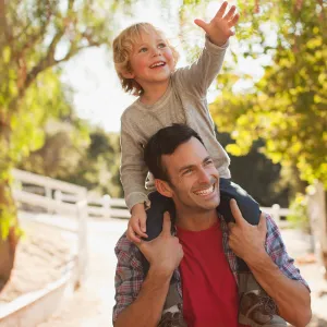 A Man Carrying His Son in a Playful Manner Over His Shoulders Through the Woods.