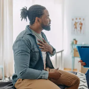 A Patient Holds His Hand to His Chest as He Consults with His Physician in a Doctor's Office.