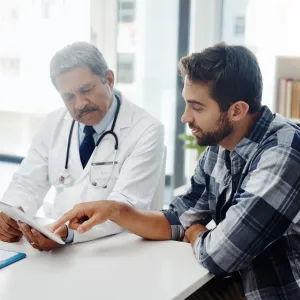 A Doctor Reviews a Patient's Chart with Him on a Tablet in His Office.
