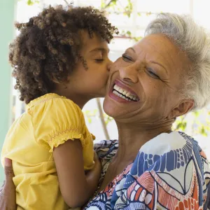 A grandmother holding her grandchild, who is giving her a kiss on the cheek.