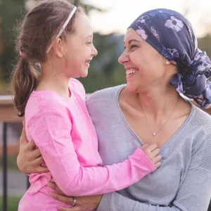 A mother and cancer survivor is sitting, with one arm around her daughter.