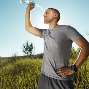 A man outside, post run, squirting water on his face