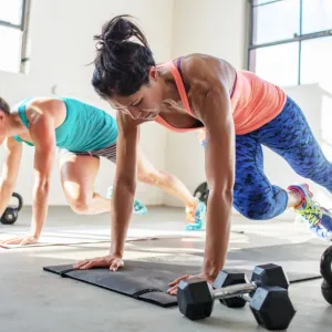 Two women side by sided, working out on mats on the ground