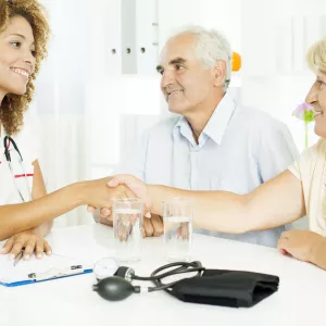 Senior couple discussing heartburn with their doctor. They are all sitting at a table and the doctor is grasping hands with the wife.