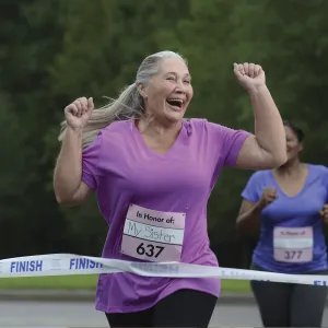 An older woman is ecstatic as she crosses the finish line of a charity foot race