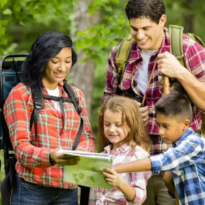 A family reads a map together while hiking in the woods.