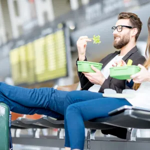 A young couple sitting in the airport lounge, eating healthy meals.