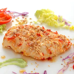 a serving of prepared chicken, coated in sesame seeds and surrounded by shredded cabbage