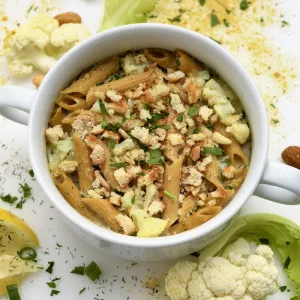 White bowl filled with cauliflower-pasta next to garnishes