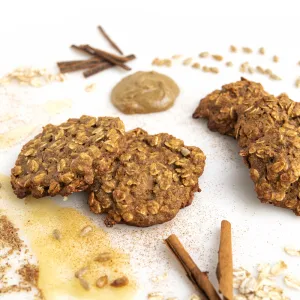 Five oatmeal cookies on a white surface with cinnamon sticks