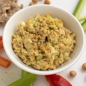 White bowl of chickpea chicken-style salad with vegetable stick garnishes