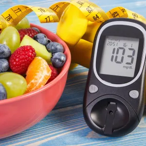 A bowl of fresh fruit next to a blood sugar monitor