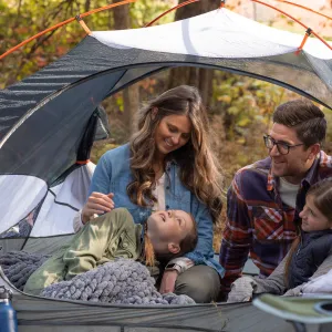 Mom, Dad and two little girls sitting in a tent cuddling in the forest