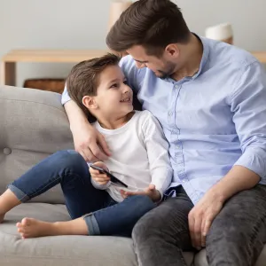 A father talks to his son on the living room couch.