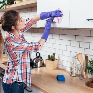 A young woman cleans the cabinets in her kitchen