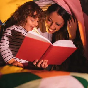 A mom and daughter read together by flashlight.