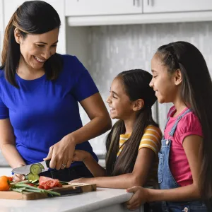 A mom chopping vegetables with her daughters in the kitchen.