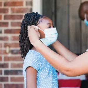 A mom helps her daughter with her face mask.