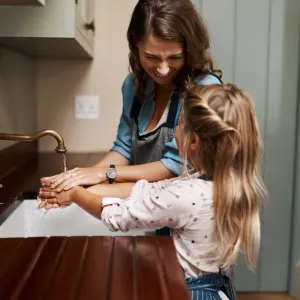 A mother and daughter wash their hands at the kitchen sink.