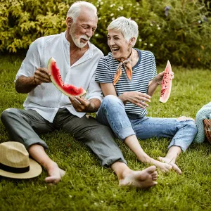 A couple eating watermelon at an outdoor picnic.