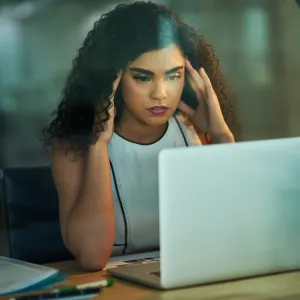 A woman massaging her temples at her desk at work.