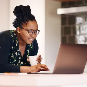 A black woman researches on her laptop while drinking coffee