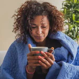 An adult black woman sips tea at home on her couch