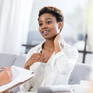 A young woman rubs her neck as she talks to a nurse