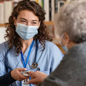 Hospice worker with mask talking to elderly patient