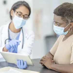 Doctor talking with patient about results on tablet, wearing masks