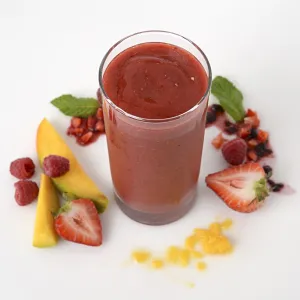 a tall glass of smoothie, surrounded by chopped mango and mixed berries