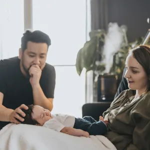 Mother with her baby on her lap and father placing his hand on his baby's head while at home together.