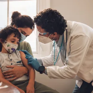 A mother holds her son while a doctor prepares to administer a vaccine.