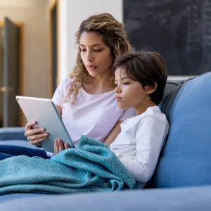 A mother and son sitting on a couch and using a tablet.