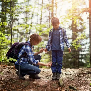 A mother spraying her son with bug spray while on a hike in the woods.