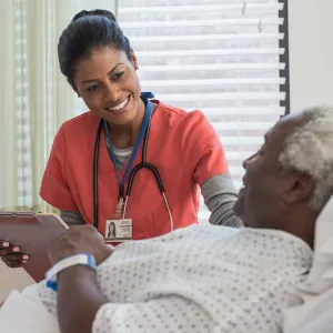 Nurse holding clipboard and standing by elderly patient's bedside