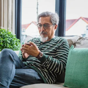 Older man sitting on a couch at home using a phone.