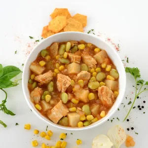 Dish of chicken and vegetable stew surrounded by assortment of veggies and garnish