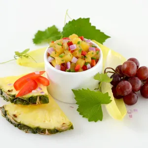 Dish of pineapple and jalapeno salsa surrounded by grapes and greens