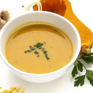 Bowl of squash soup with half butternut squash and green sprig garnish on side