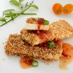 Two and a half crusted tofu steaks with herb and tomato garnishes