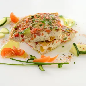 two slices of a veggie-packed omelet, surrounded by additional slices of zucchini and tomato 